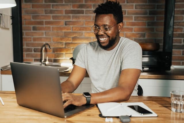 Person with glasses working at a desk on their laptop in front of a brick wall